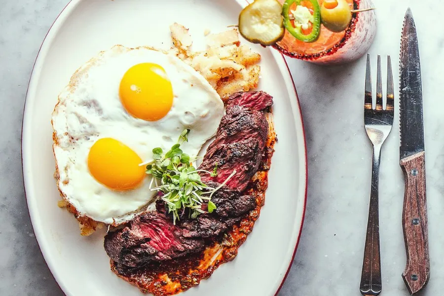 Steak and eggs over potatoes with a cocktail on the side
